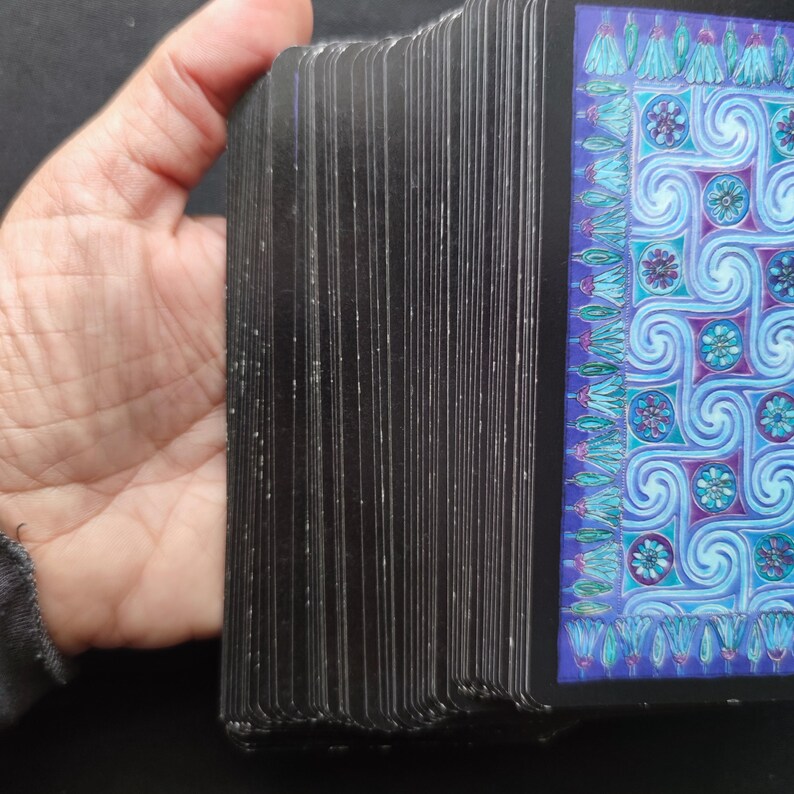 Dos des cartes divinatoires tenues en main, tranches visibles et traces d’usure apparentes.